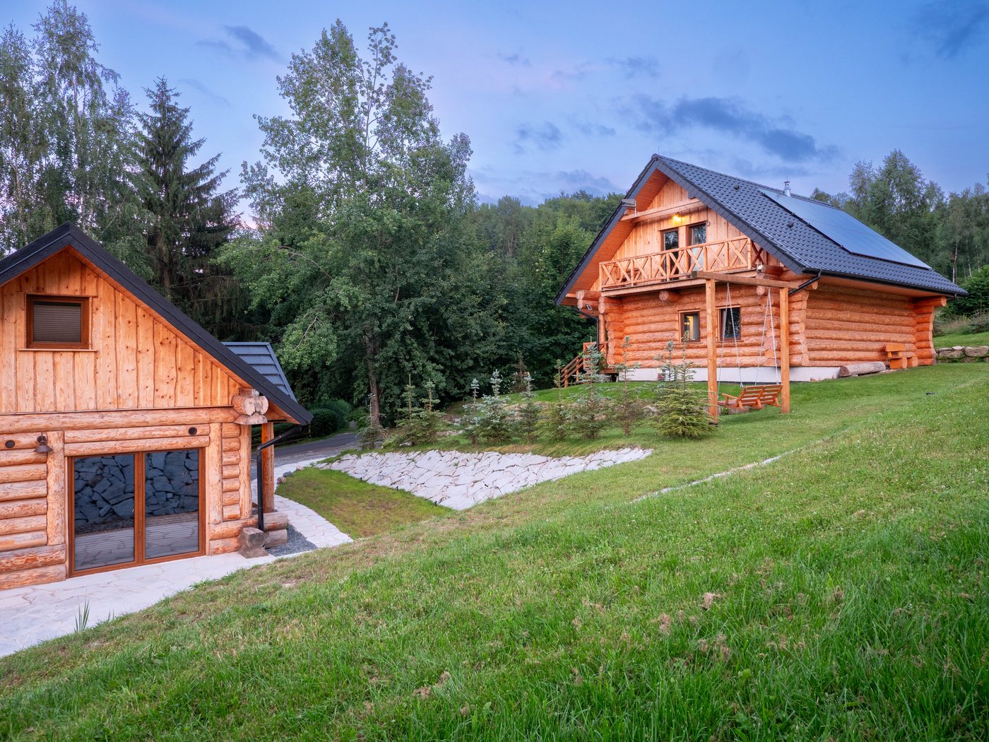 Dom z bali o zmierzchu, huśtawka na trawie